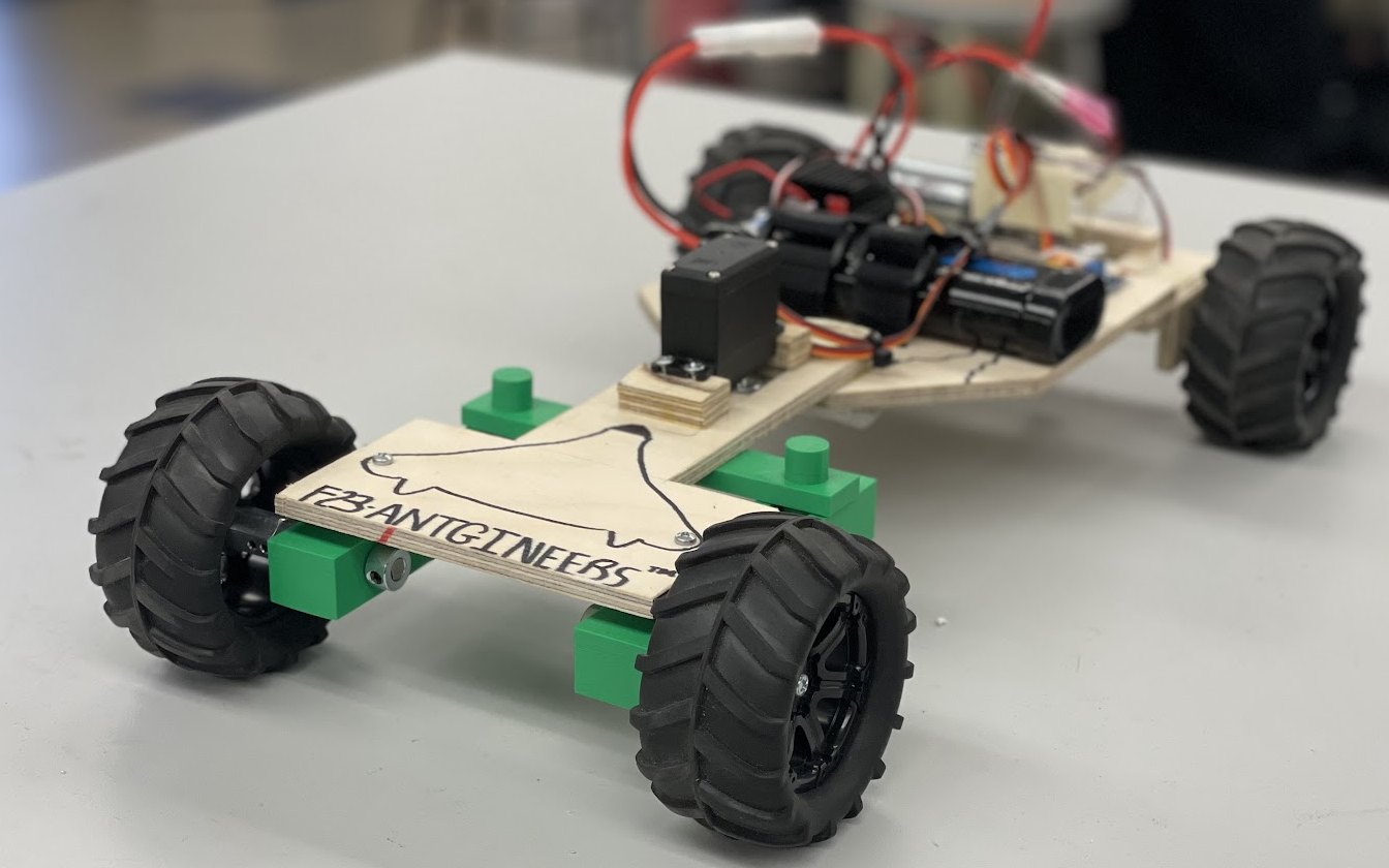 The finished rover on a workbench: a plywood chassis carrying the Antgineers logo, four off-road wheels on green 3D-printed mounts, with the servo, battery, motor and receiver on the rear deck