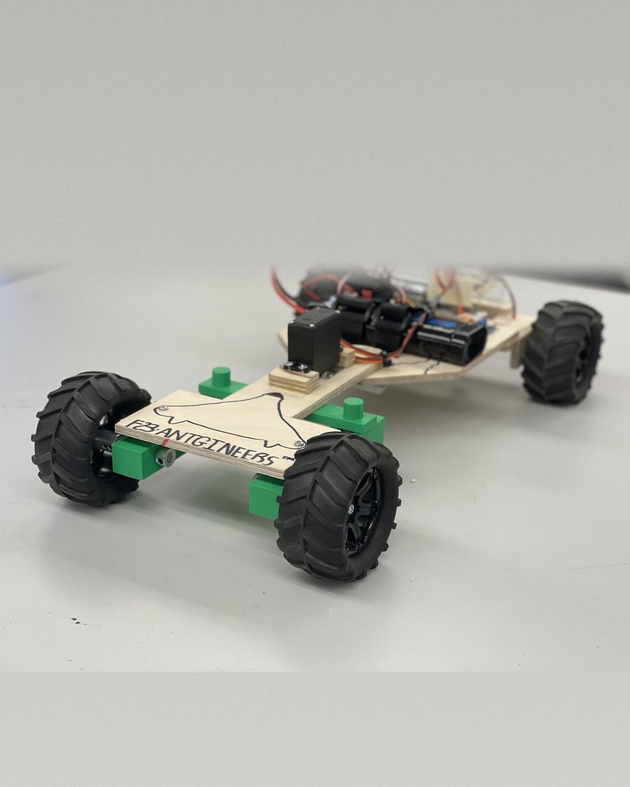The Antgineers RC rover: a plywood chassis carrying the team logo, four off-road wheels on green 3D-printed mounts, with the servo, battery and motor on the rear deck