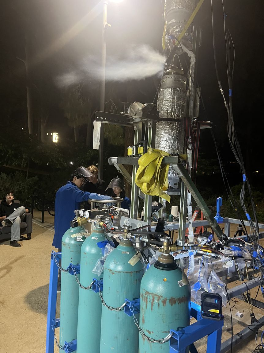 The vertical test stand venting vapor at night during a cold flow, crew in face shields working at the K-bottle manifold
