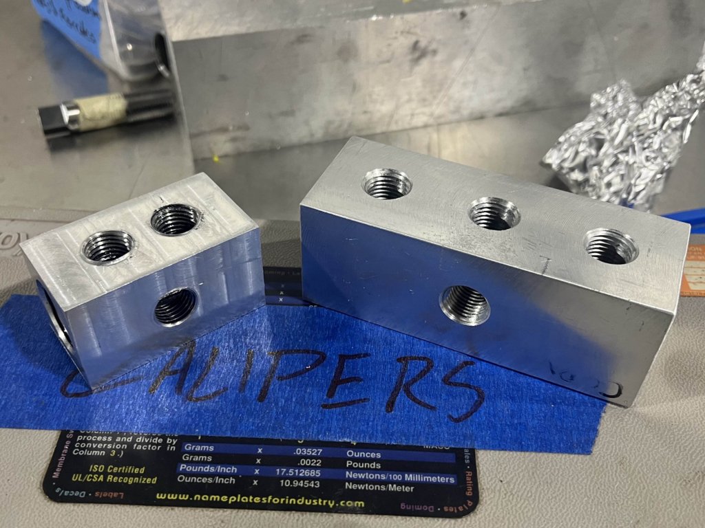 Two of the machined aluminum manifold blocks on a workbench, drilled and tapped with threaded ports