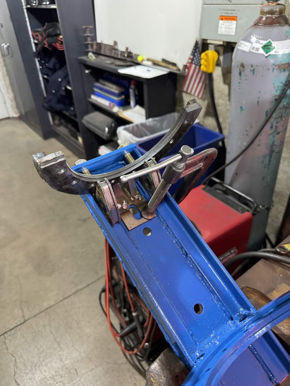The welded steel engine mount clamped in a fixture with its machined saddle bracket, on a cart in the machine shop