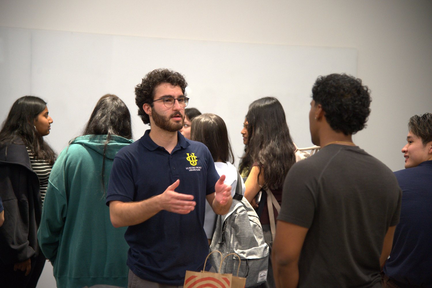 Aras in a UCI Rocket Project polo speaking with a group of students at an indoor information session