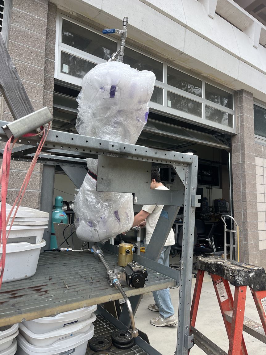 The venturi wrapped in plastic sheeting on a test rig with buckets below, mid water test against a building wall