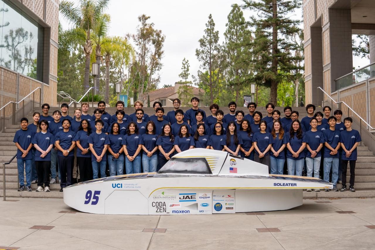 The UCI solar car team on campus steps behind the car's aerobody, a low white shell numbered 95 and lettered SOLEATER