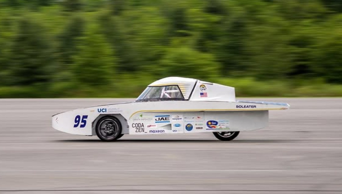 The finished solar car, numbered 95 and lettered SOLEATER, running at speed on a track with a motion-blurred treeline behind it
